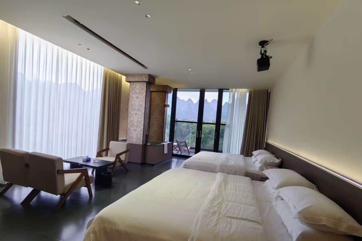 Habitación de hotel con una cama grande, un escritorio con silla y vistas a las montañas desde la ventana.