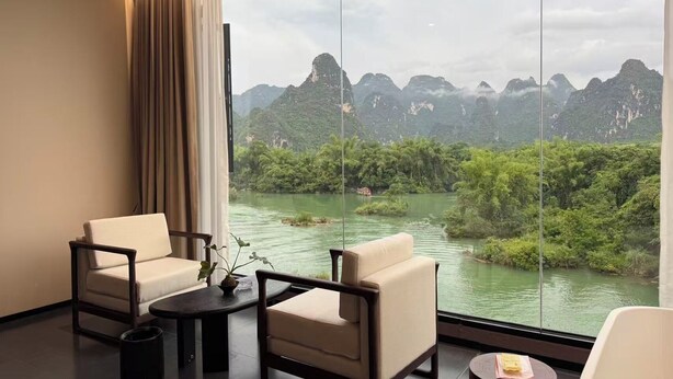 A room with two chairs, a small table, and a view of a river and mountains.