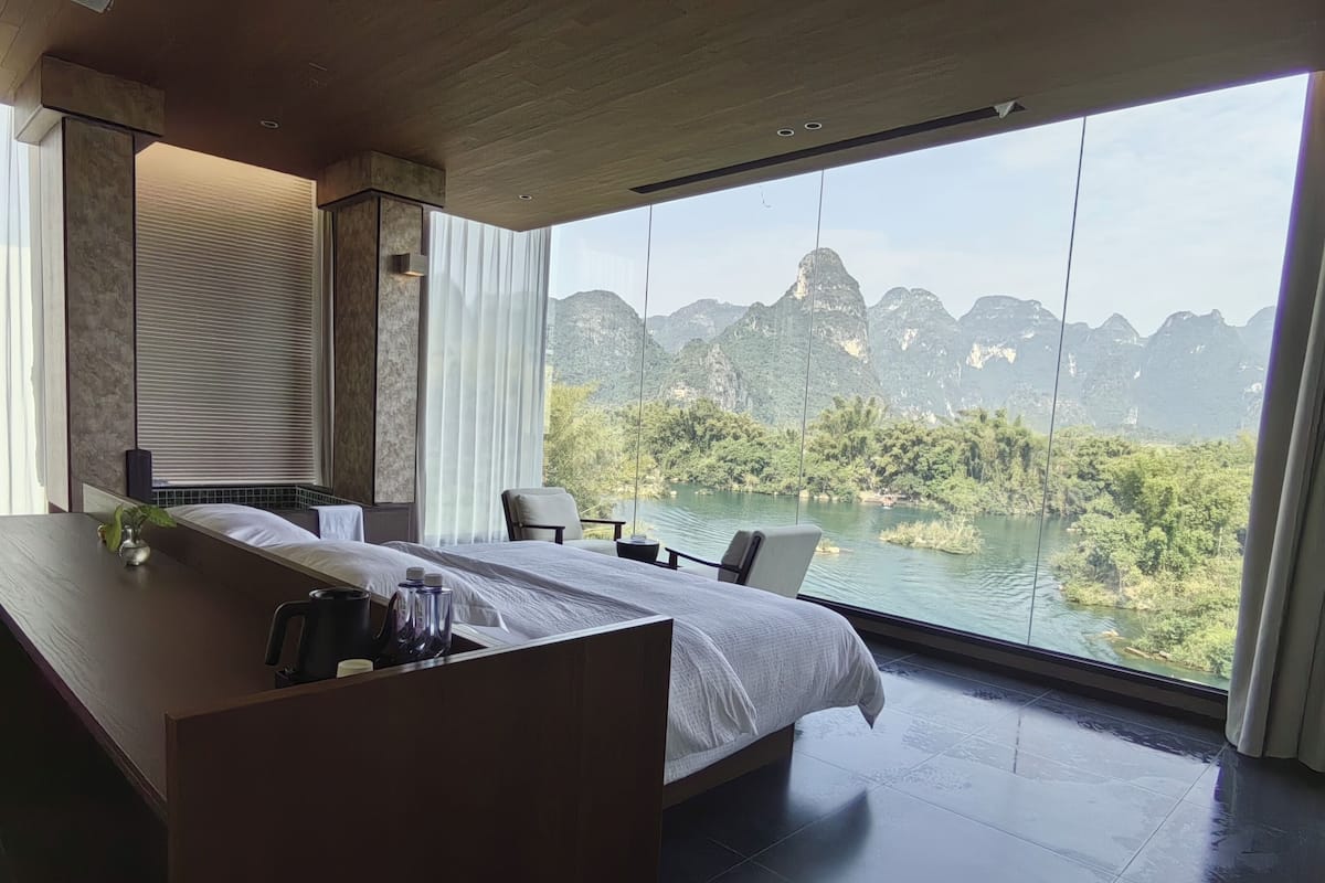 Habitación de hotel moderna con una cama grande, un escritorio y vistas a un lago y montañas.