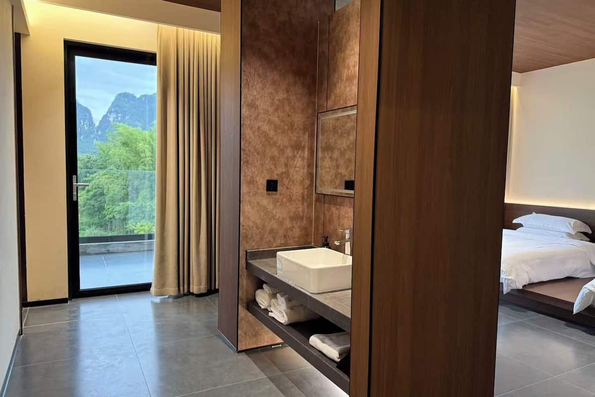 Habitación de hotel moderna con un ventanal grande, un lavamanos integrado, un espejo y una cama con ropa de cama blanca.