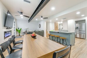 A modern kitchen with a central island, bar stools, a dining table with chairs, a built-in TV, and a large window.