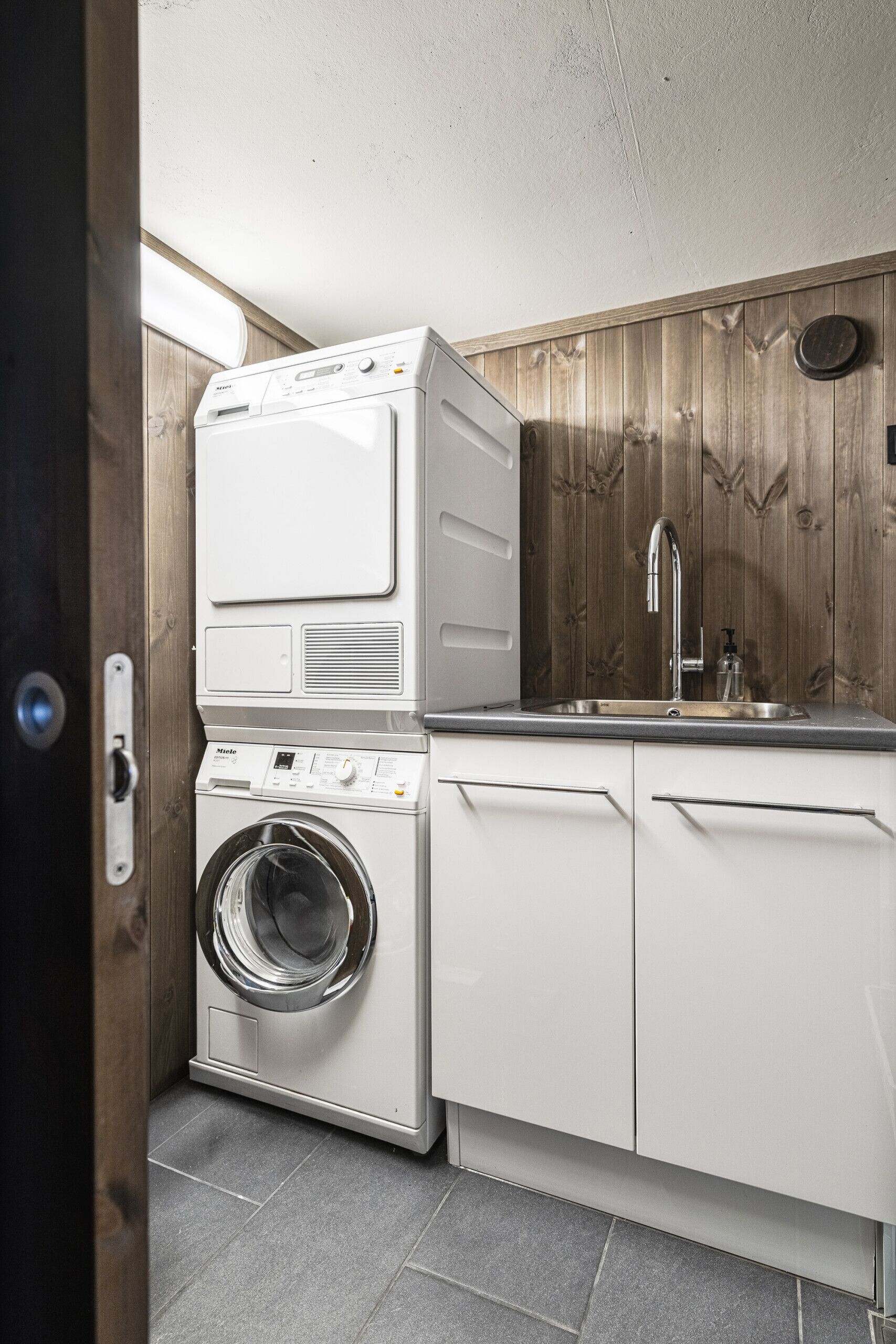 Ein kleiner Waschbereich mit Waschmaschine und Trockner, einem Waschbecken und Holzvertäfelung an der Wand.