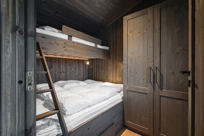 A wooden bunk bed with a ladder, a wardrobe, and a small shelf above the bed.