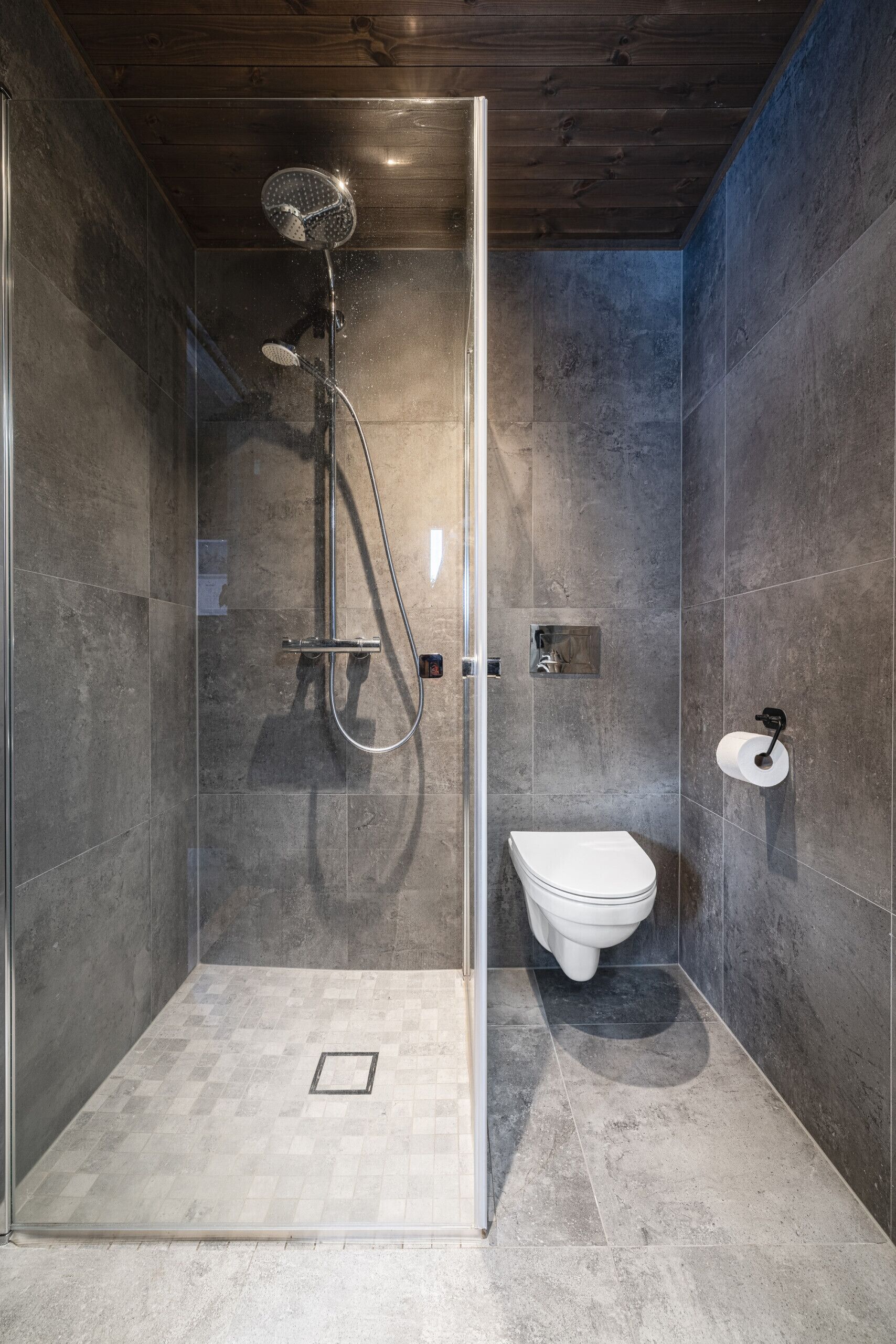 A modern shower with a glass door, a white toilet, and a small shelf with toiletries.