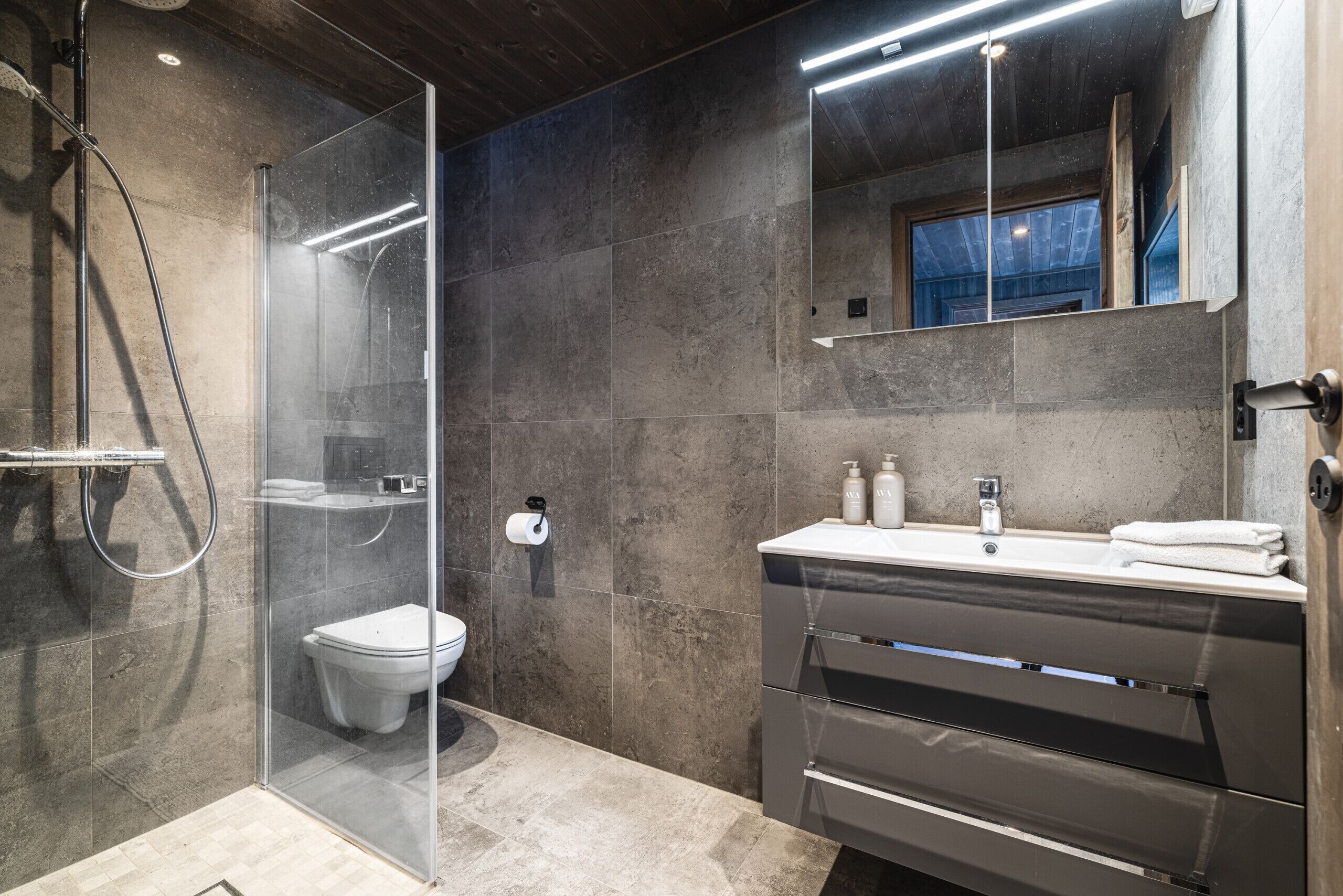 Un baño moderno con cabina de ducha de vidrio, inodoro, tocador con espejo y un perchero para toallas.