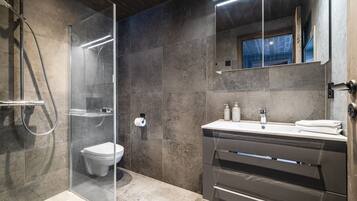 Un baño moderno con cabina de ducha de vidrio, inodoro, tocador con espejo y un perchero para toallas.