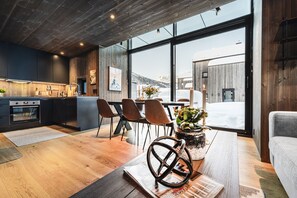 A modern kitchen with wooden accents, a dining area with chairs, and a large window offering a view of the outside.