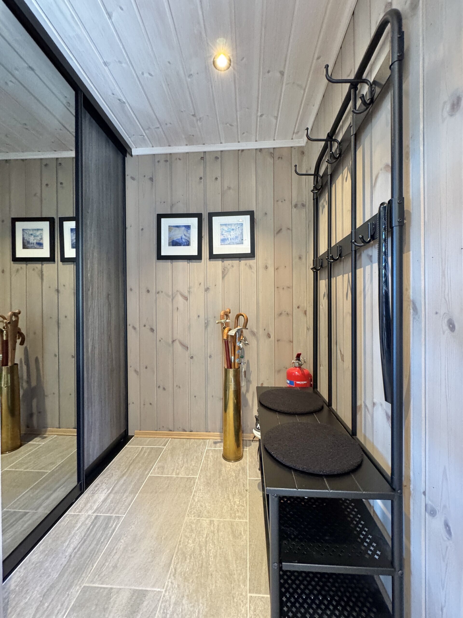 A room with wooden walls, a black metal bench, a fire extinguisher, and framed pictures on the wall.