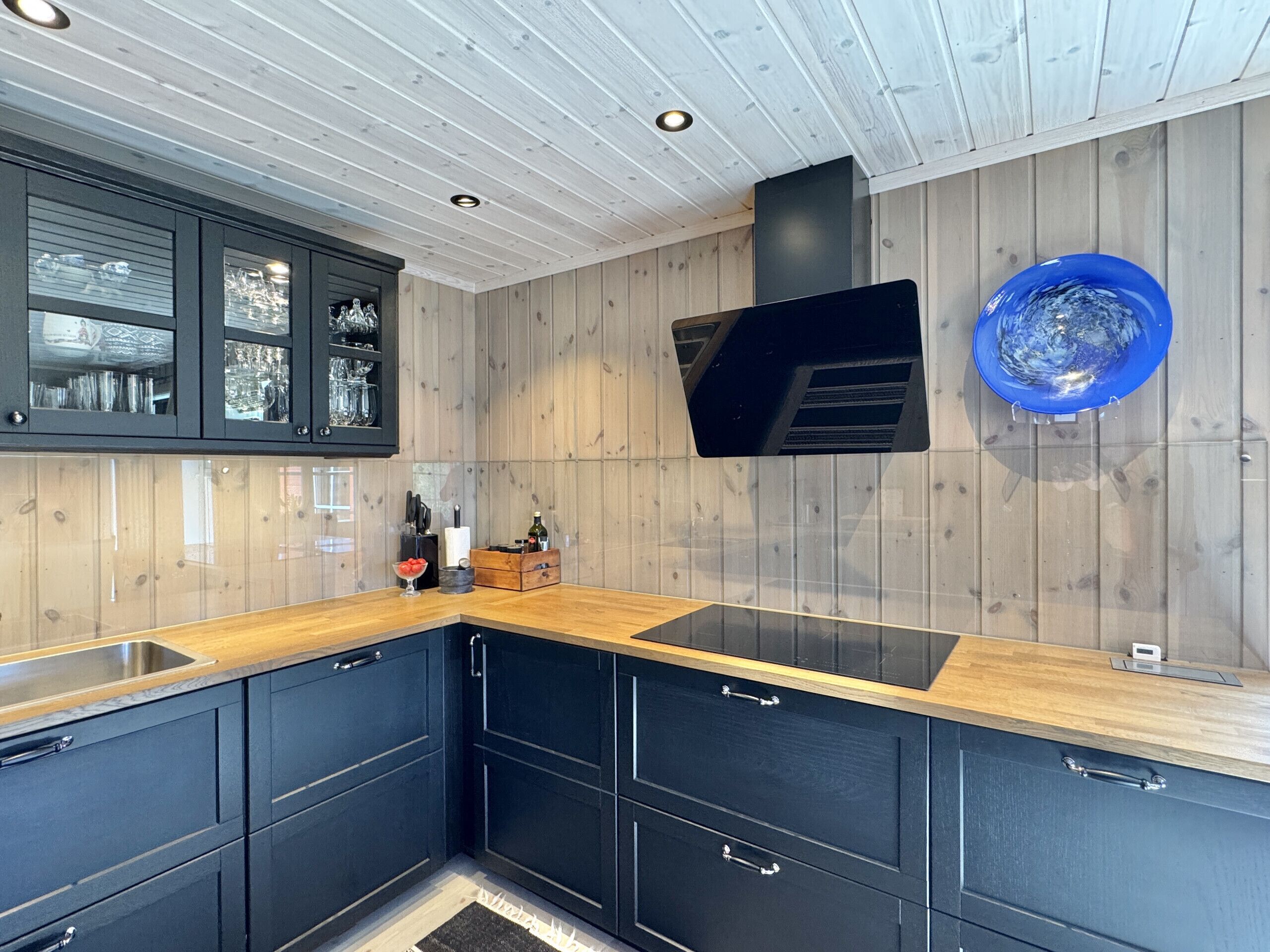 A modern kitchen with dark cabinets, a wooden countertop, and a built-in TV.