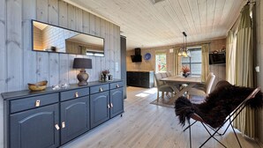 A modern kitchen with wooden cabinets, a dining area with a table and chairs, and a large mirror above the counter.
