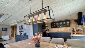 A modern kitchen with dark cabinets, a wooden dining table, and a hanging light fixture.