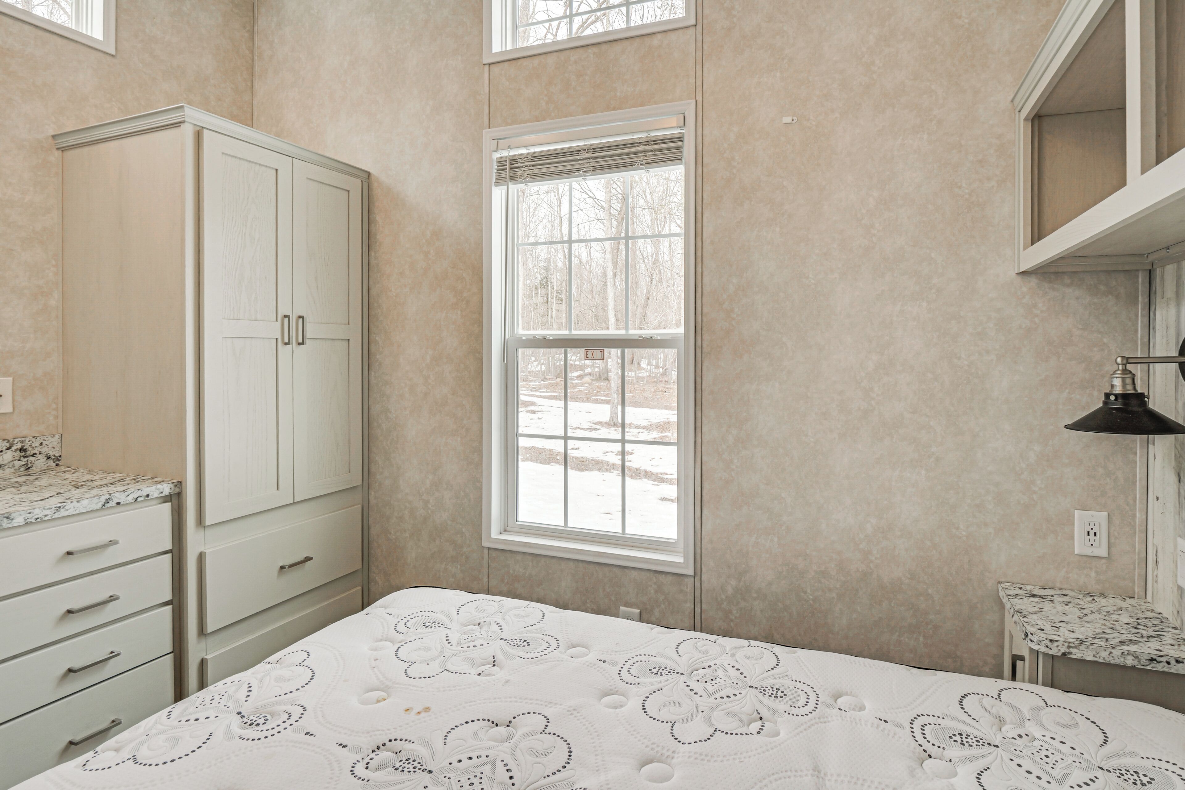 A bedroom with a bed, a window, a wardrobe, and a small table.