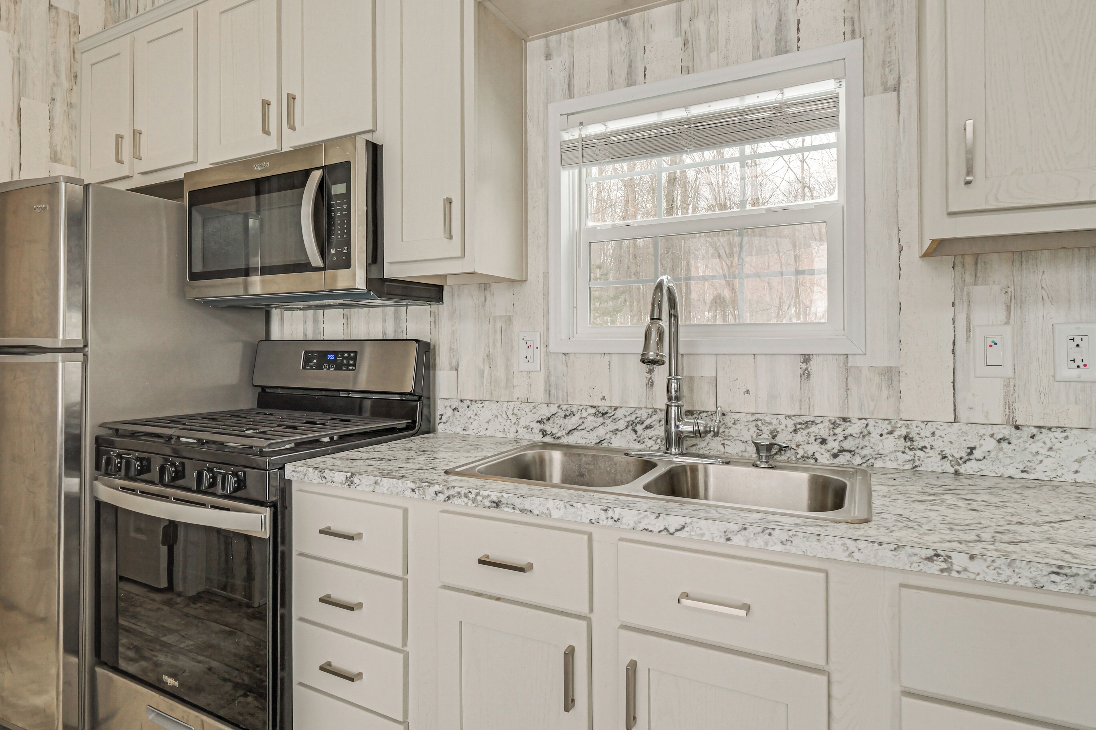 Una cocina con armarios blancos, un refrigerador de acero inoxidable, un microondas, una estufa y un lavamanos doble.