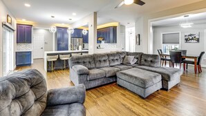 Una sala de estar moderna con un sofá modular, un comedor y una cocina al fondo.