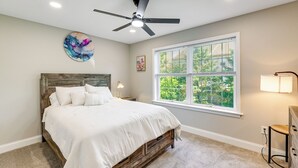 Un dormitorio con cama, ventilador de techo, ventana con persianas y mesita de noche.
