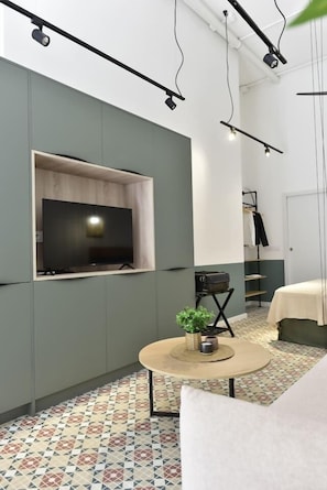 A modern room with a flat-screen TV mounted on a wall, a round coffee table with a plant, and a patterned floor. - Loft-style studio in La Petxina (Valencia)