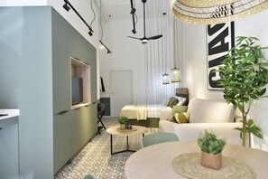 A modern living room with a sofa, a small round table, and a TV mounted on a wall. - Loft-style studio in La Petxina (Valencia)