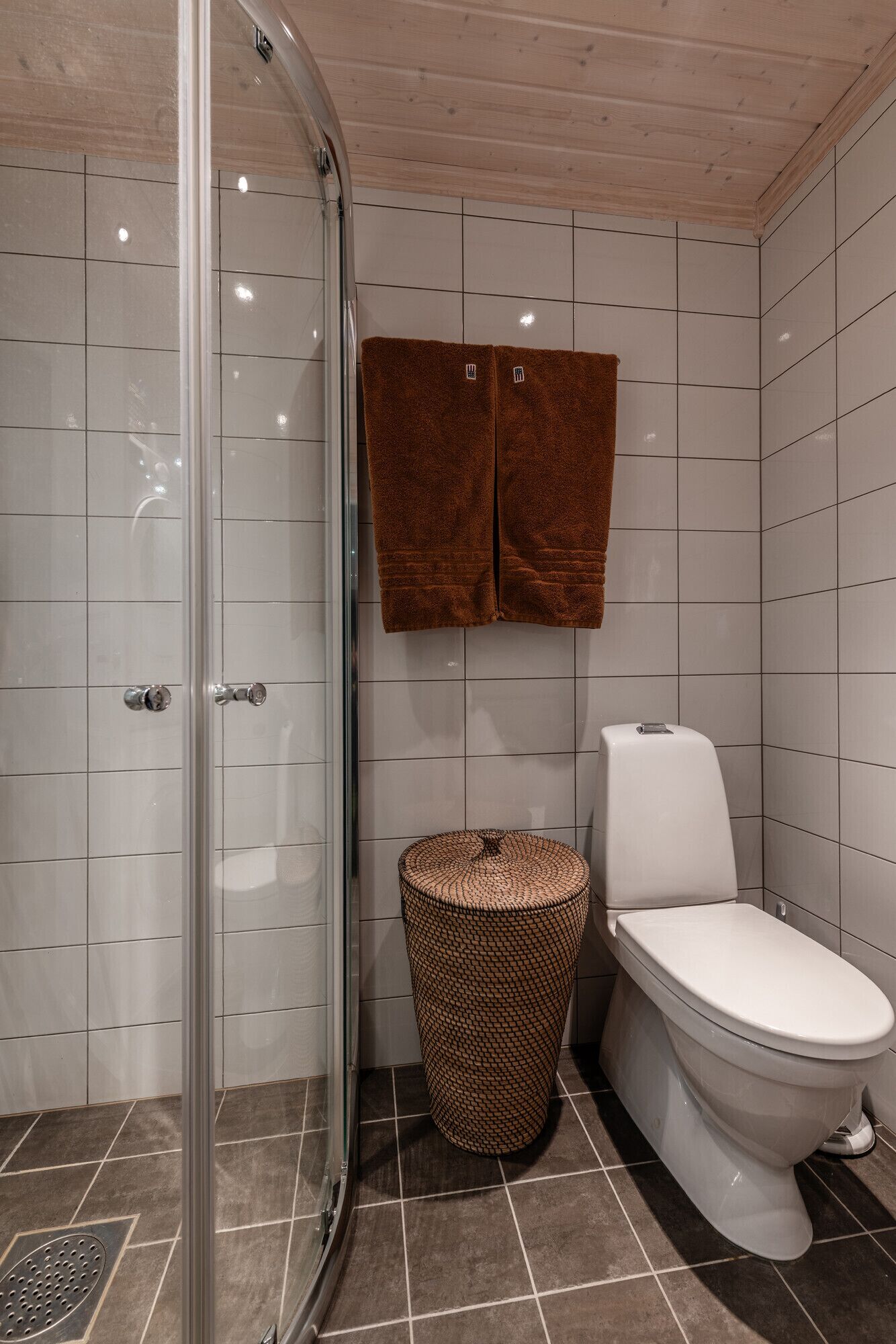 Un baño con cabina de ducha de vidrio, inodoro y un cesto de mimbre.