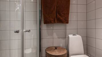 Un baño con cabina de ducha de vidrio, inodoro y un cesto de mimbre.