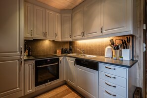 A kitchen with white cabinets, a dishwasher, an oven, a sink, and a countertop with a knife block. - Geilotunet Apartment (Hol)