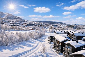 A snow-covered village with wooden buildings, a clear sky, and a sun shining. - Geilotunet Apartment (Hol)