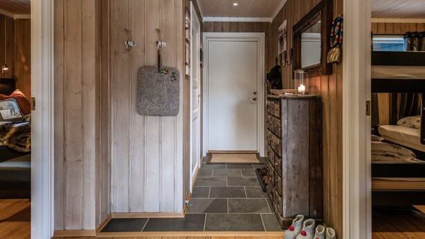 Ein Holzflur mit Steinwand, einer Tür, einem Schuhregal und einem Bett im Hintergrund.