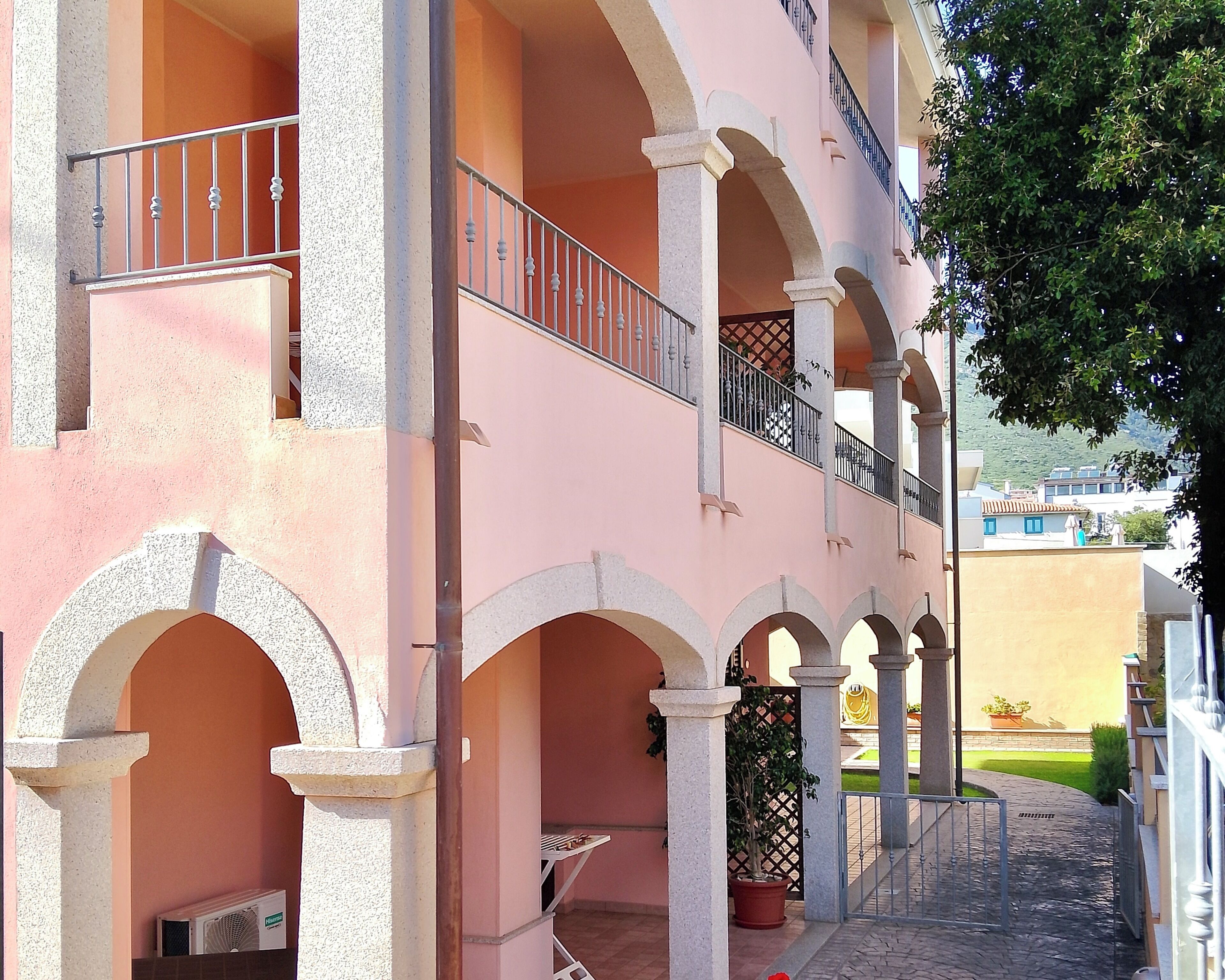 A multi-story building with balconies, a covered outdoor area with a grill, and a paved walkway.