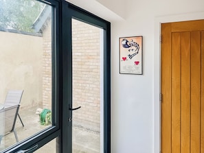An open door leading to a patio with a brick wall, a framed poster on the wall, and a wooden door to the right.