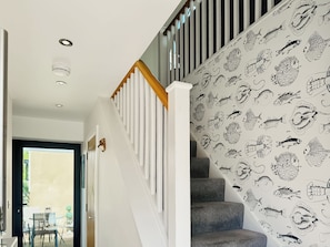 Una escalera con barandilla blanca y peldaños grises que conduce a una habitación con techo blanco e iluminación empotrada.