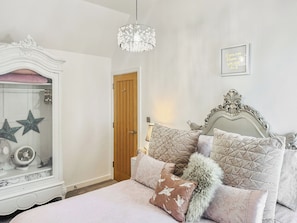 A bedroom with a bed, a white wardrobe, a wooden door, a chandelier, and a motivational quote on the wall.