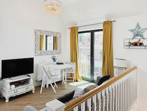 A modern living room with a TV, white furniture, a desk, and a staircase.