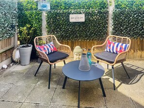 A patio area with two wicker chairs, a small round table, and a Buddha statue. - The Salt Yard Villa 3 - UK52113 (Whitstable)