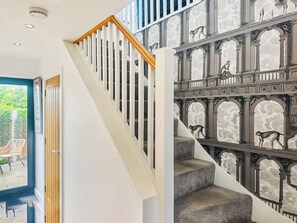 Un escalier avec une rampe blanche et une moquette grise, menant à une pièce d’où l’on peut admirer la verdure environnante.