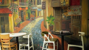 Een restaurant met een muurschildering van een straatsbeeld, tafels, stoelen en een bordje voor 'Beauty Guest House'.