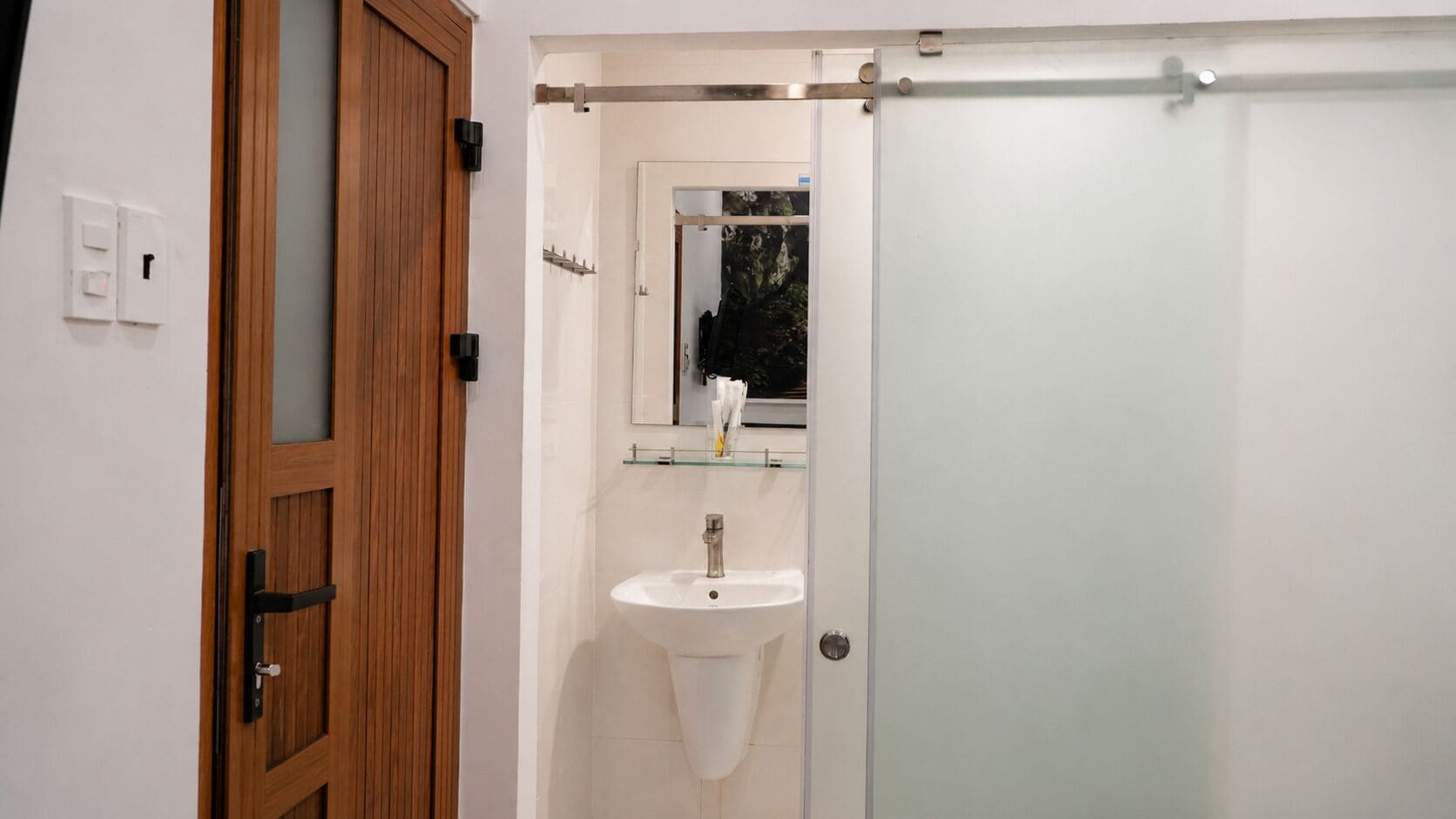 A bathroom with a wooden door, a white sink, and a glass shower enclosure.