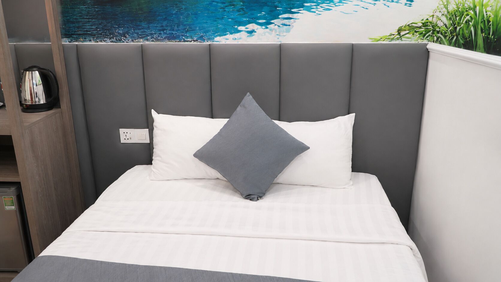 A bed with a grey upholstered headboard, white bedding, and a grey pillow.