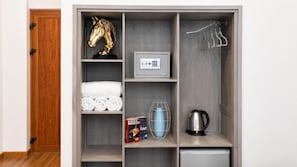 Een kast met planken met opgevouwen handdoeken, een boek, een decoratief paardenhoofd, een kluisje, een waterfles en een waterkoker.