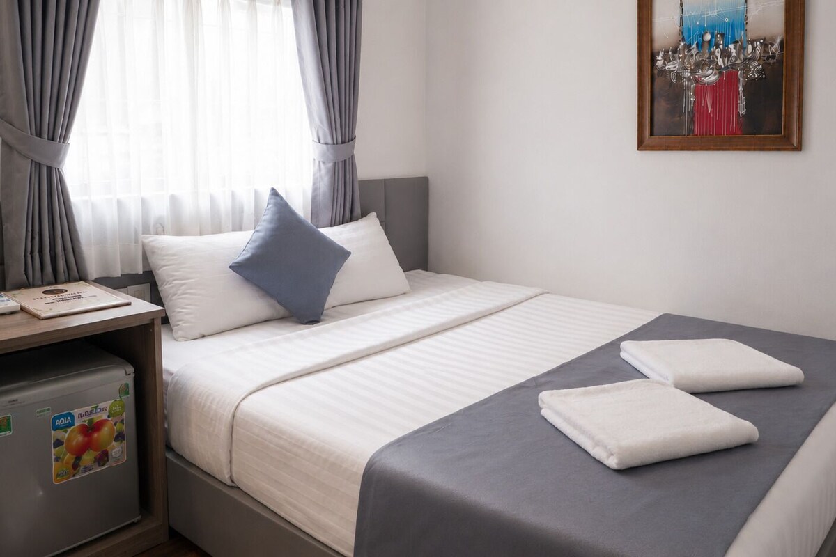Een netjes opgemaakt bed met een grijze spreidek, twee kussens en twee opgevouwen handdoeken.