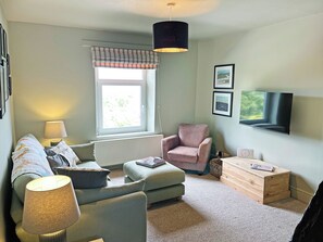 A living room with a sofa, armchair, lamp, TV, and a window with curtains.