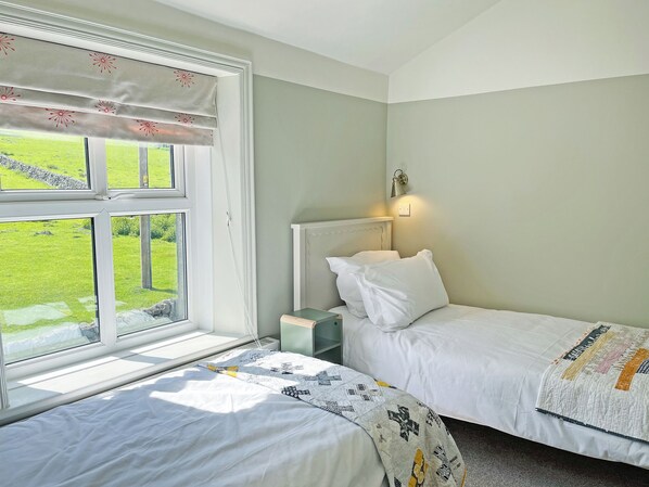A bedroom with two beds, a window with a view of a green landscape, a bedside lamp, and a quilt on one bed.