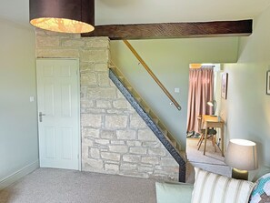 A staircase with a stone wall, a white door, a wooden beam ceiling, a lamp, a chair, and a table.