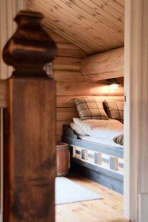 A wooden interior with a bed, pillows, a nightstand, and a lamp.
