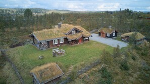 A remote cabin with a grass roof, surrounded by a grassy landscape and trees.
