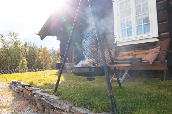 A rustic cabin with a chimney, a hanging grill, and a stone wall.