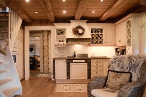 A kitchen with stone accents, wooden cabinets, a built-in wine rack, and a cozy seating area with a patterned rug.