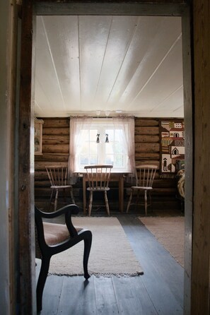 A log cabin interior with a dining table, four chairs, a rug, and a window with curtains.
