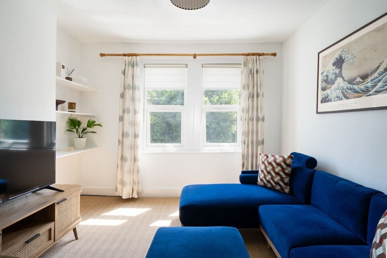 A modern living room with a blue sofa, a flat-screen TV, and a large window with curtains.
