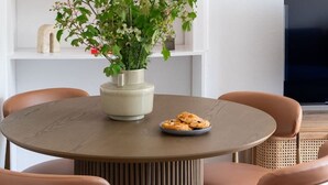 Zona pranzo con un tavolo rotondo, sei sedie, una pianta in vaso e una televisione a schermo piatto sullo sfondo.