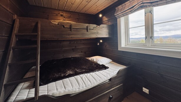 Ein Zimmer in einer Holzhütte mit einem Etagenbett, einer Halterung, einem Fenster mit Blick und einem kleinen Schreibtisch.