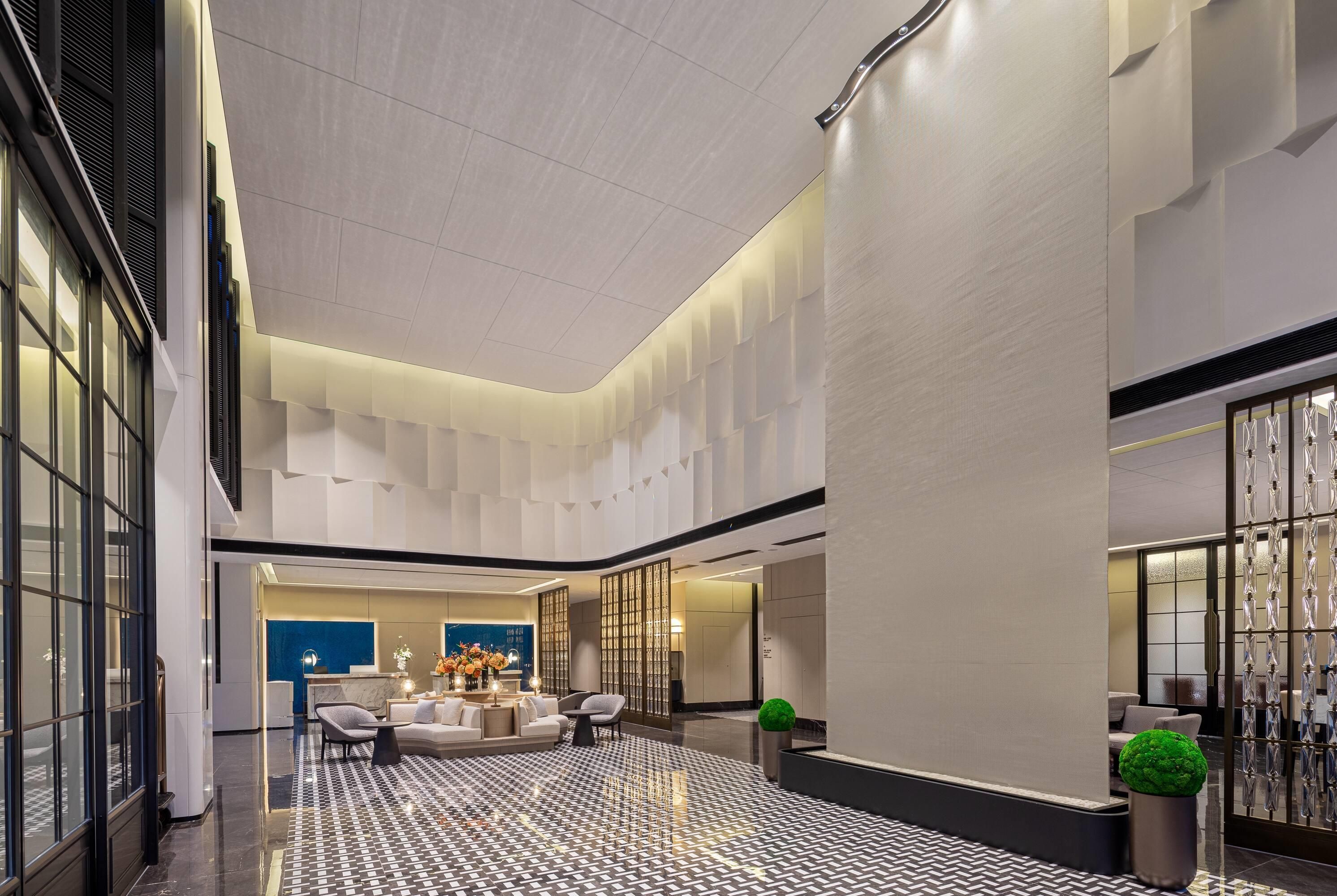A spacious lobby with a high ceiling, a reception desk, seating area, and a patterned floor.